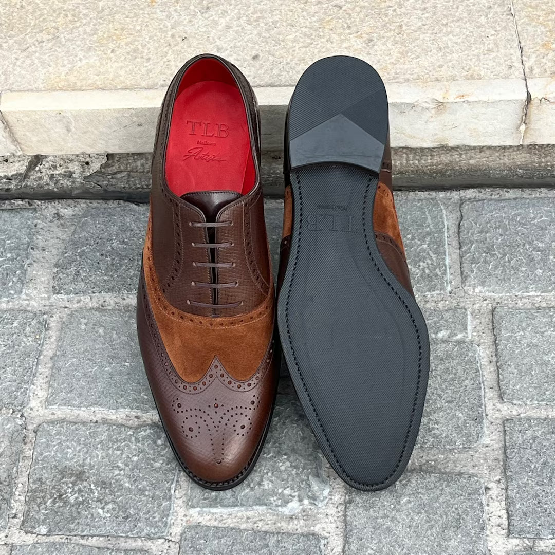 A pair of men's brogue oxford shoes shown from the top and bottom. The shoes feature dark brown leather and tan suede panels, with a bright red interior lining and a black outsole.